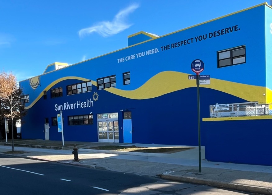 Blue and yellow Sun River Health building with the words The care you need. The respect you deserve.