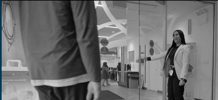 A Sun River Health staff member smiles as she holds the door open for a patient